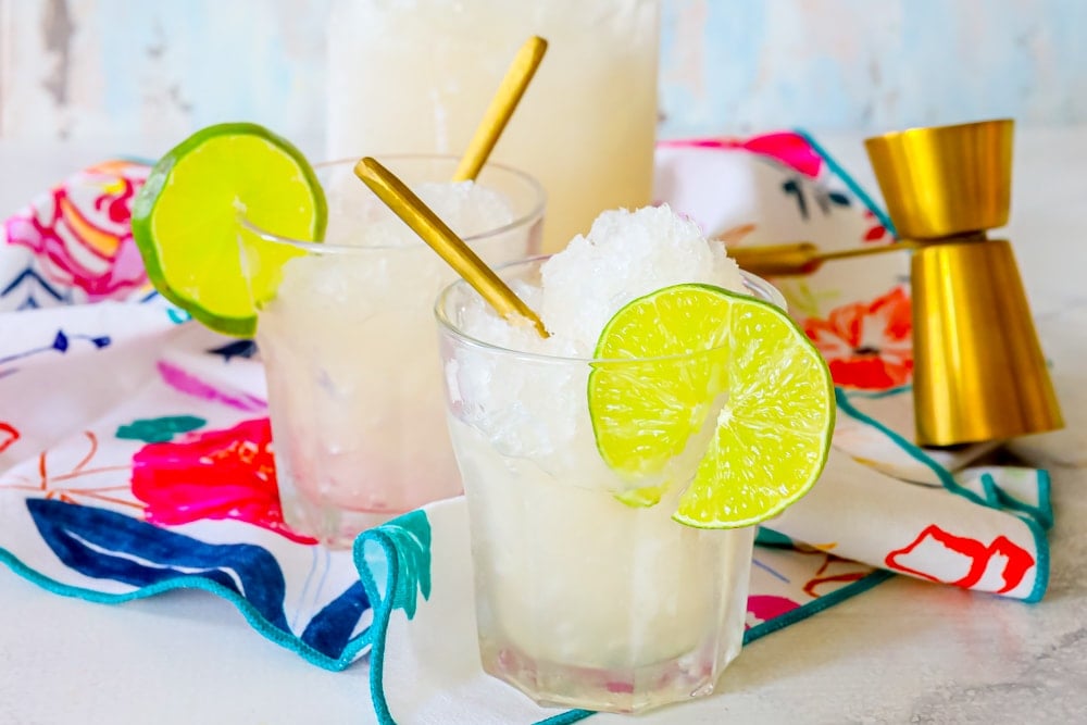 picture of two glasses with gin and tonic frozen slush, a spoon, and a lime slice in them 