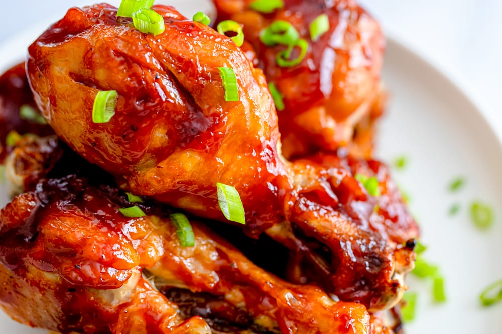 bbq chicken legs on a plate with green onions sliced on it 