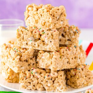 A stack of cereal bar treats on a plate with a glass of milk.