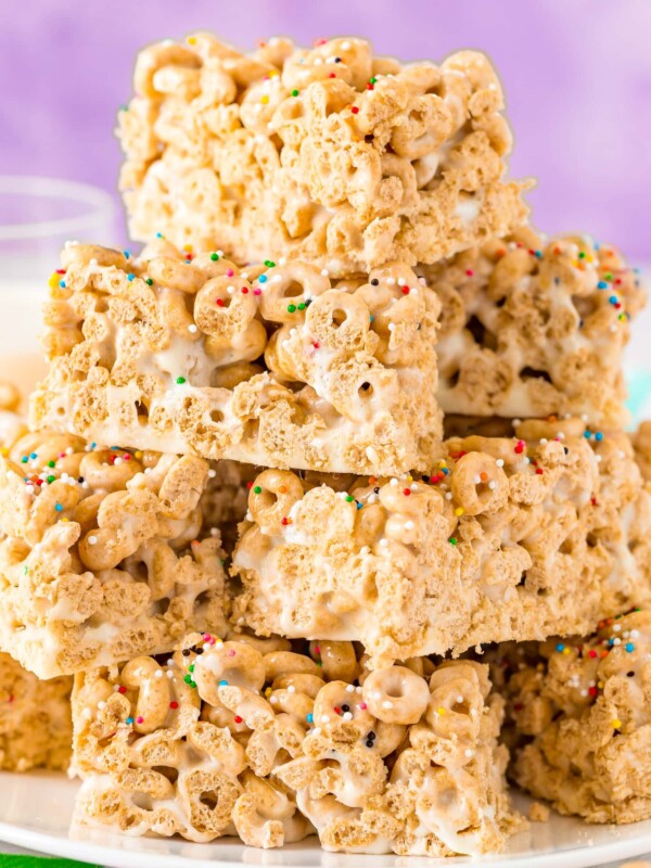 A stack of cereal bar treats on a plate with a glass of milk.