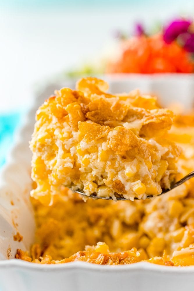 scalloped corn casserole on a spoon over a casserole dish with baked scalloped corn