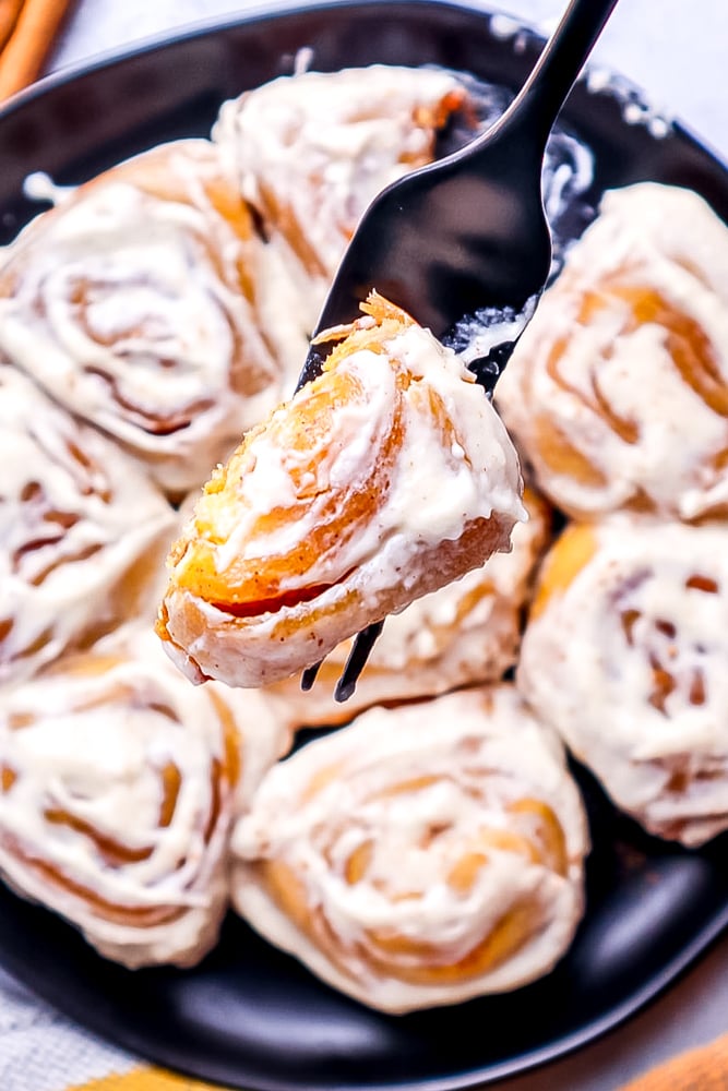 picture of a fork with cinnamon roll with a bite out of it