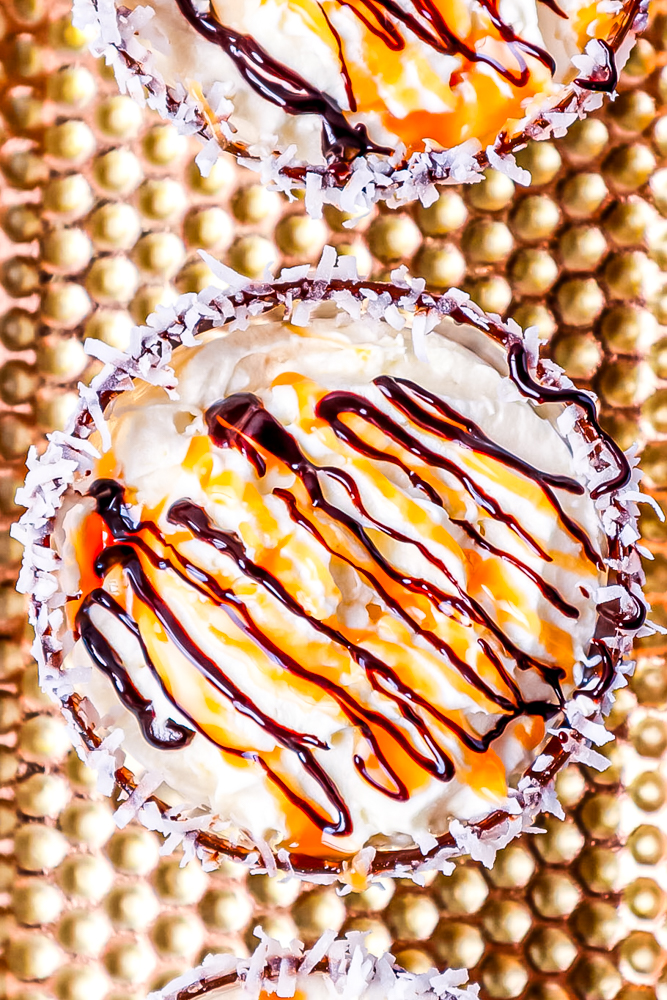 cocktail in a glass with whipped cream, caramel and chocolate sauce drizzled on top, in a glass rimmed with chocolate and coconut flakes