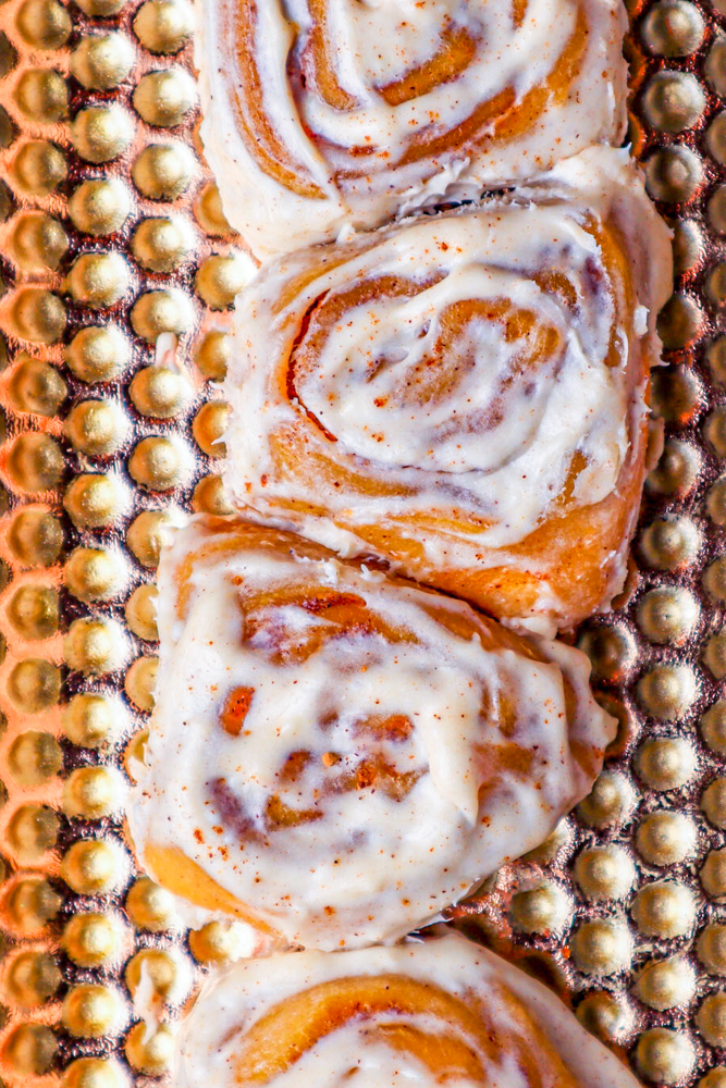 pumpkin cinnamon rolls sitting longways on a golden plate that has lots of perforations.