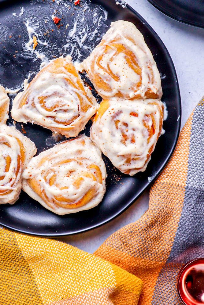 pumpkin cinnamon rolls sitting in a black pan with a checkered fall color hand towel