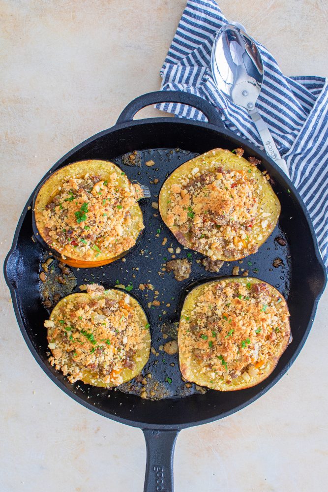 Sausage-stuffed acorn squash recipe, elegantly presented in a cast iron skillet.