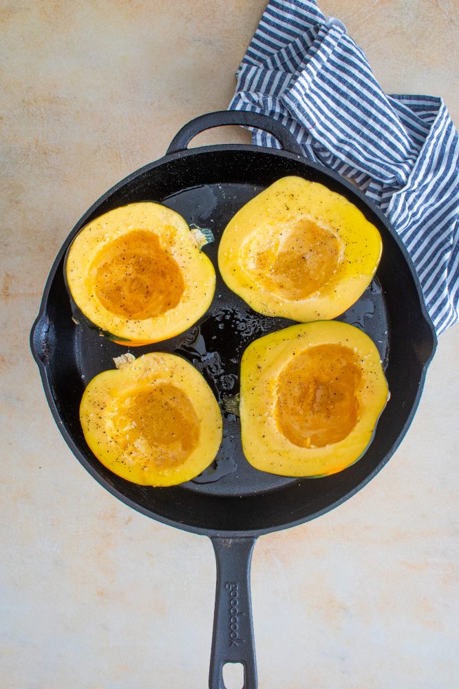 Roasted acorn squash in a cast iron skillet, ready for stuffing.