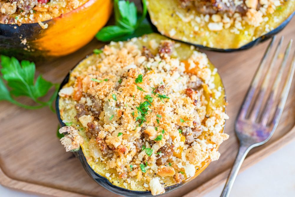 Baked sausage-stuffed acorn squash on a wooden cutting board.