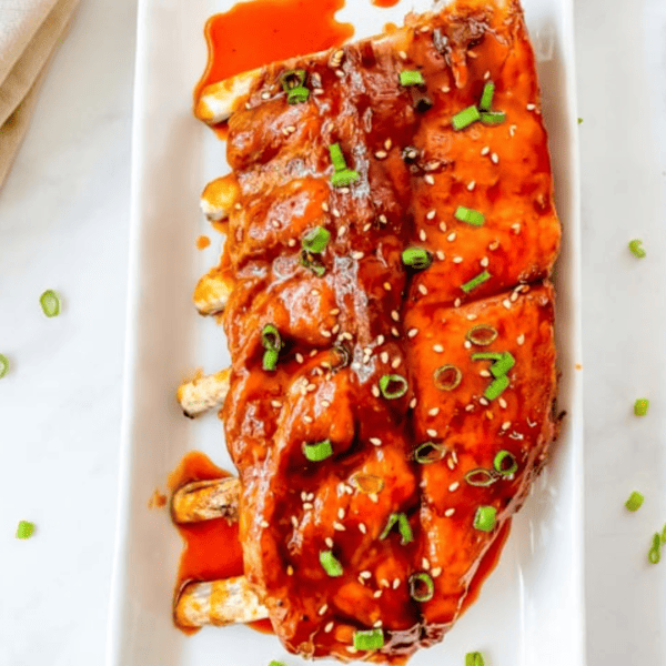 Asian Instant Pot Ribs with sauce and green onions on a white plate.
