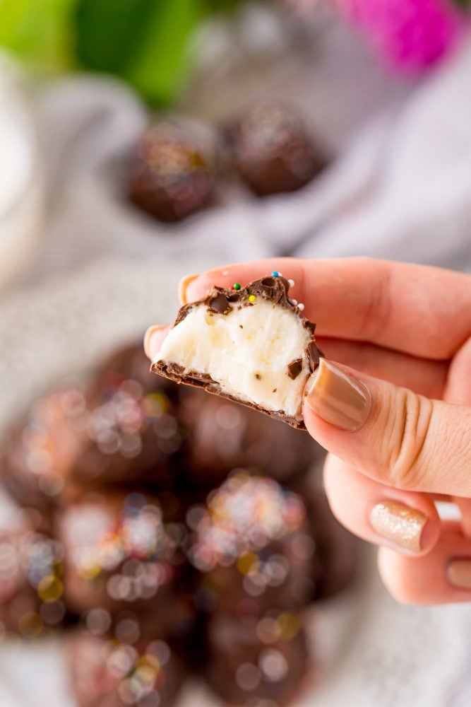 buttercream candies dipped in chocolate with sprinkles on a white plate with a bite out of it