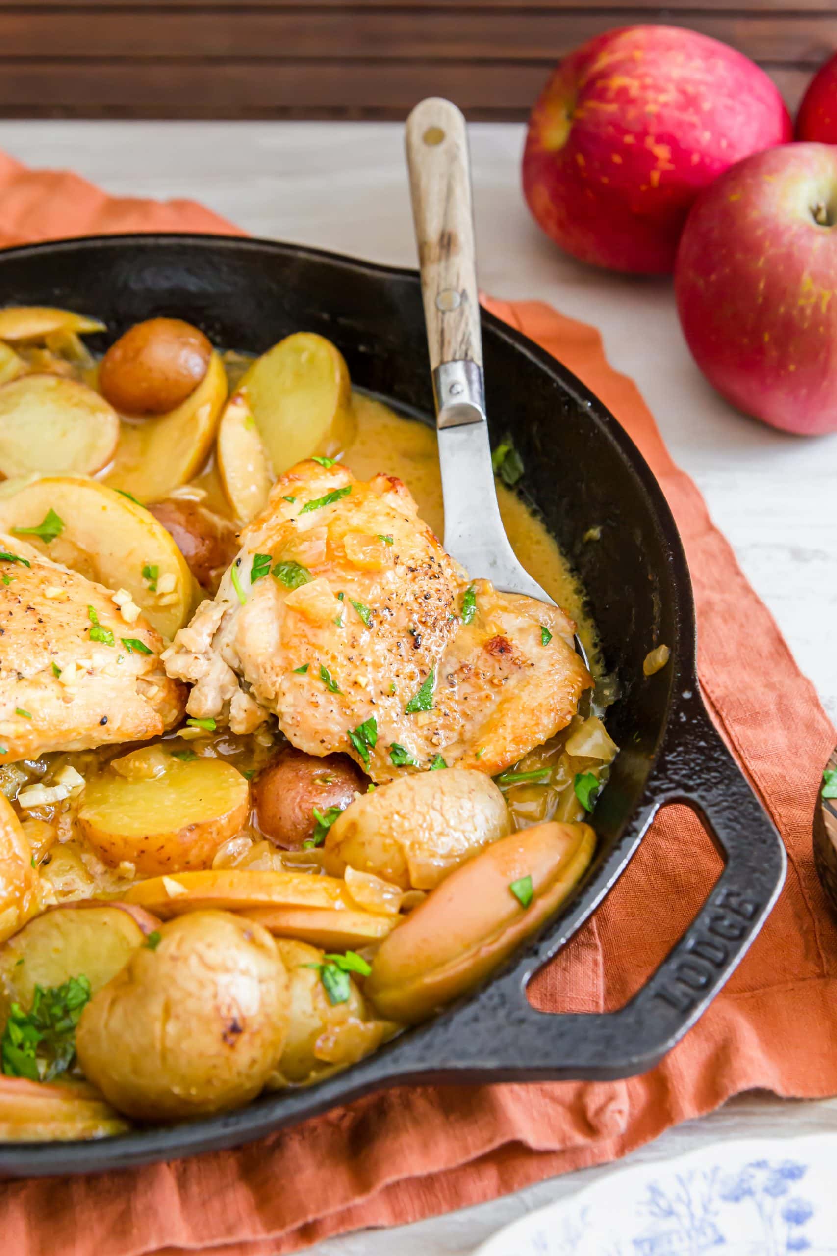 picture of chicken thigh, potatoes, apple slices in a mustard sauce in a pan 
