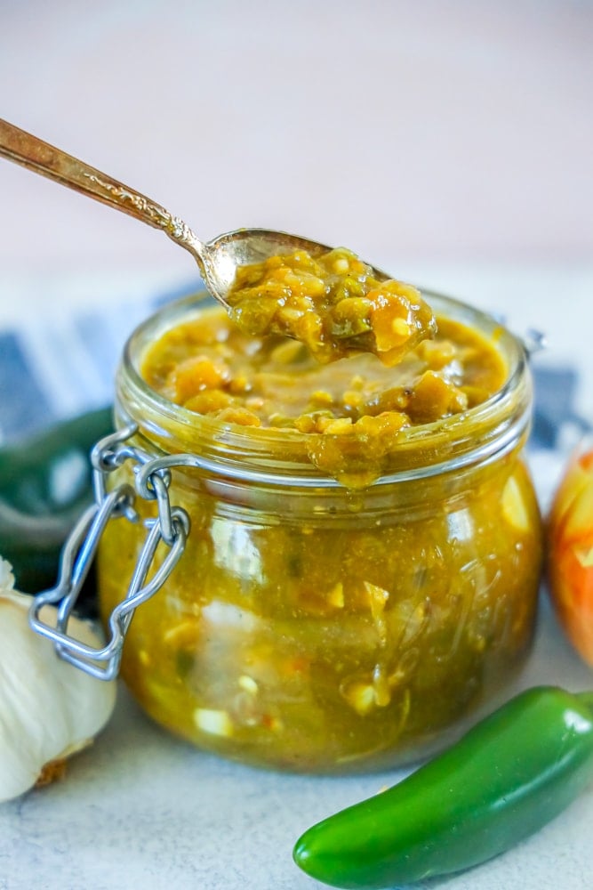 green chile sauce in a jar and a spoonful of green chile sauce in front of it