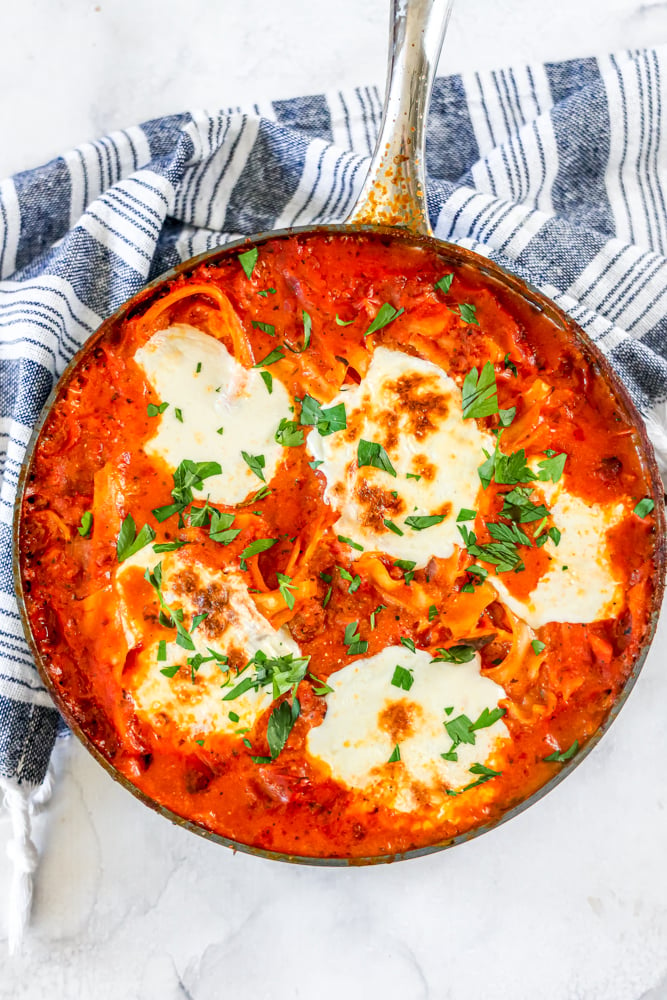 a skillet of lasagna noodles, sauce, and mozzarella cheese with parsley on it