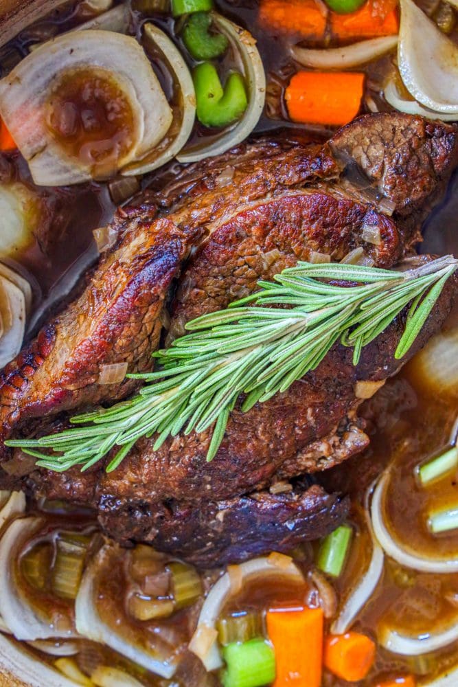 pot roast in dutch oven with gravy, celery, onion, carrots, and rosemary