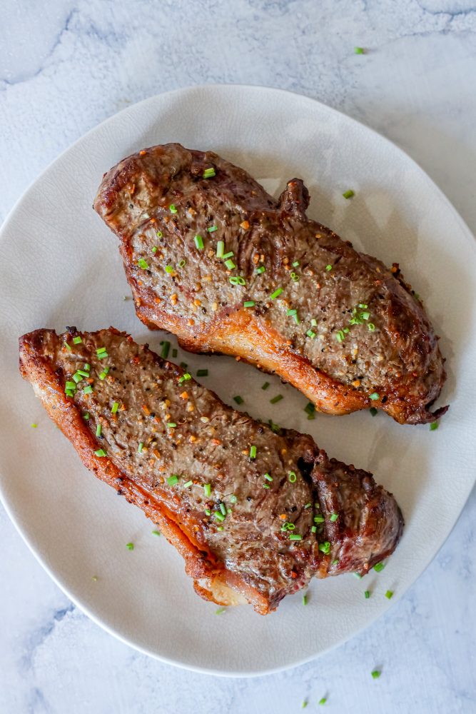 picture of two steaks on a white plate with chives 