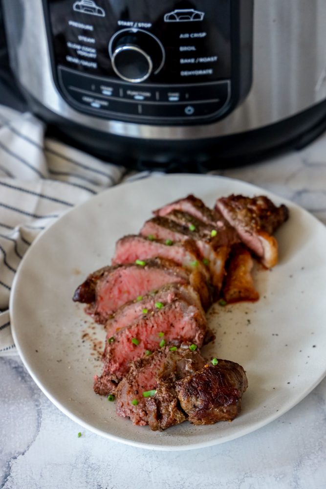 picture of medium rare sliced new york strip steak on a plate in front of an instant pot