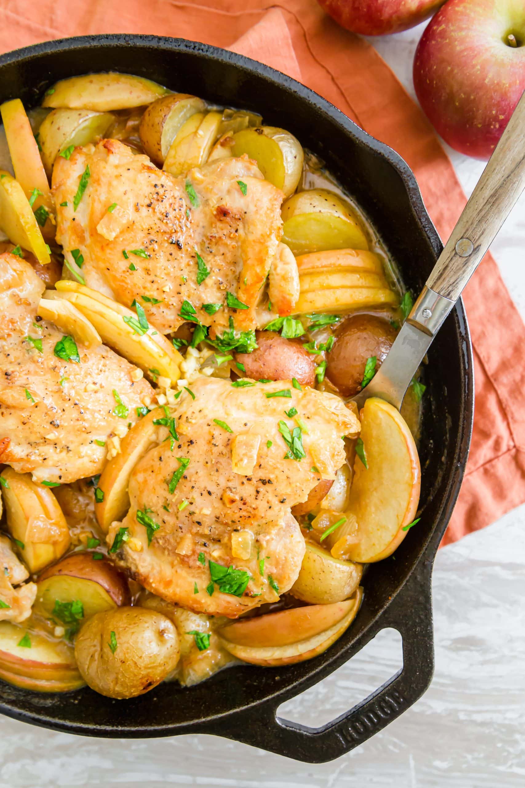 potatoes apples and chicken in a skillet on a white table with apples on it