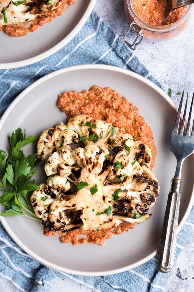 picture of a cauliflower steak with red pepper sauce on a plate with a fork