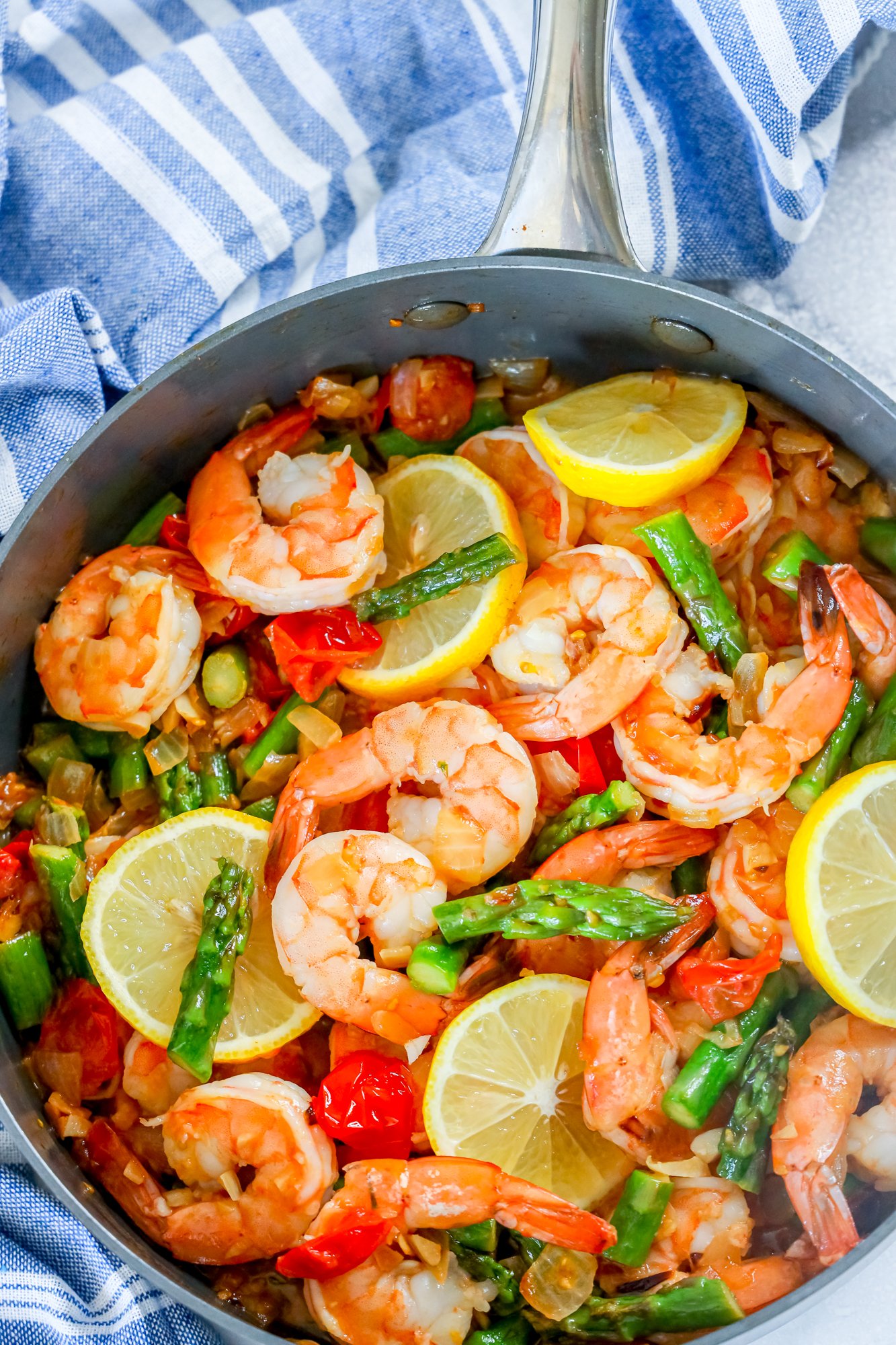 picture of shrimp, asparagus, cherry tomatoes, and lemons in a grey skillet