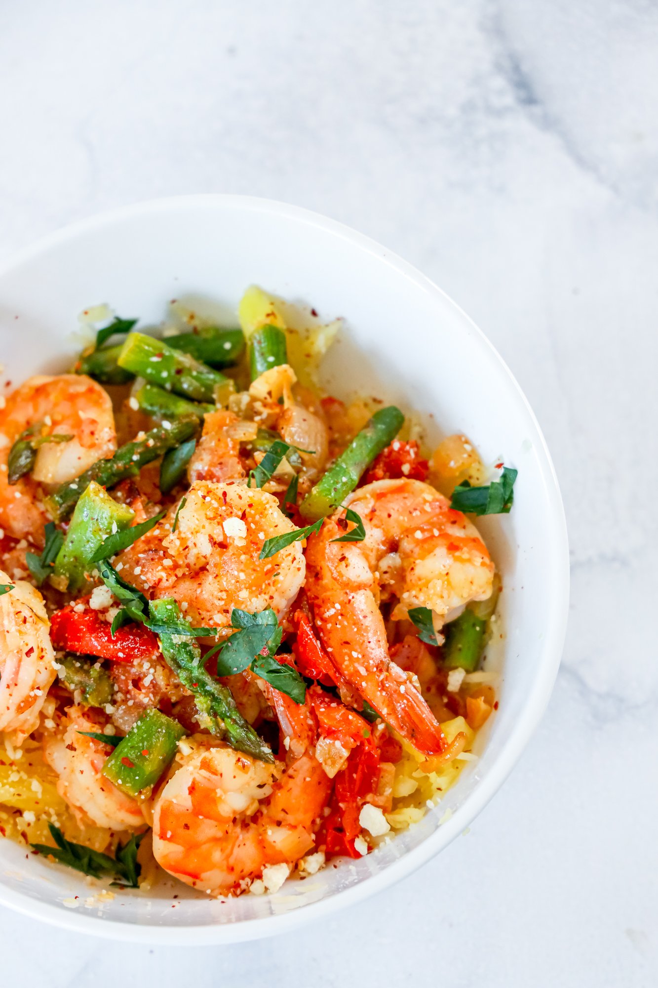 shrimp and asparagus over spaghetti squash noodles in a white bowl 