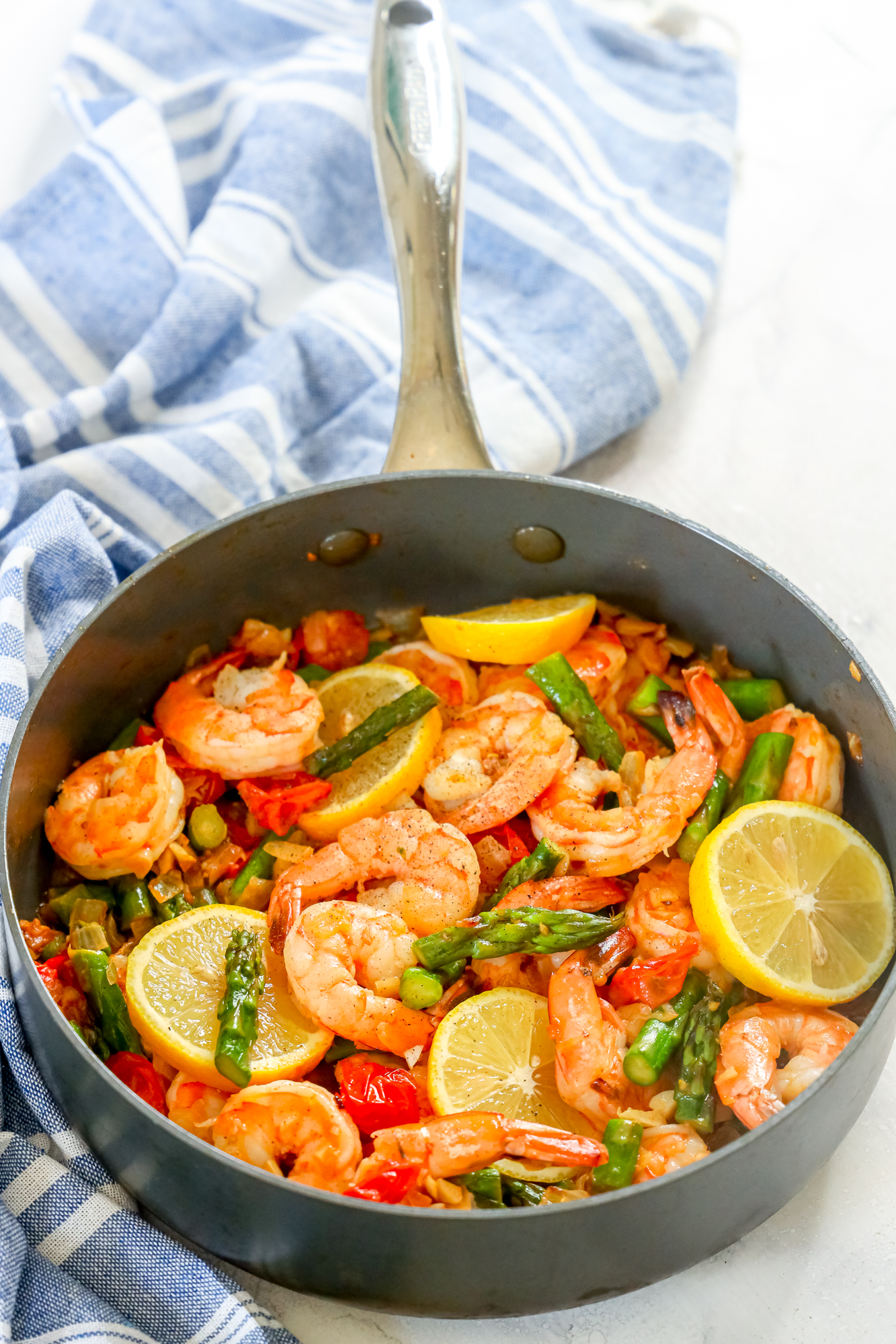 picture of shrimp, asparagus, cherry tomatoes, and lemons in a grey skillet