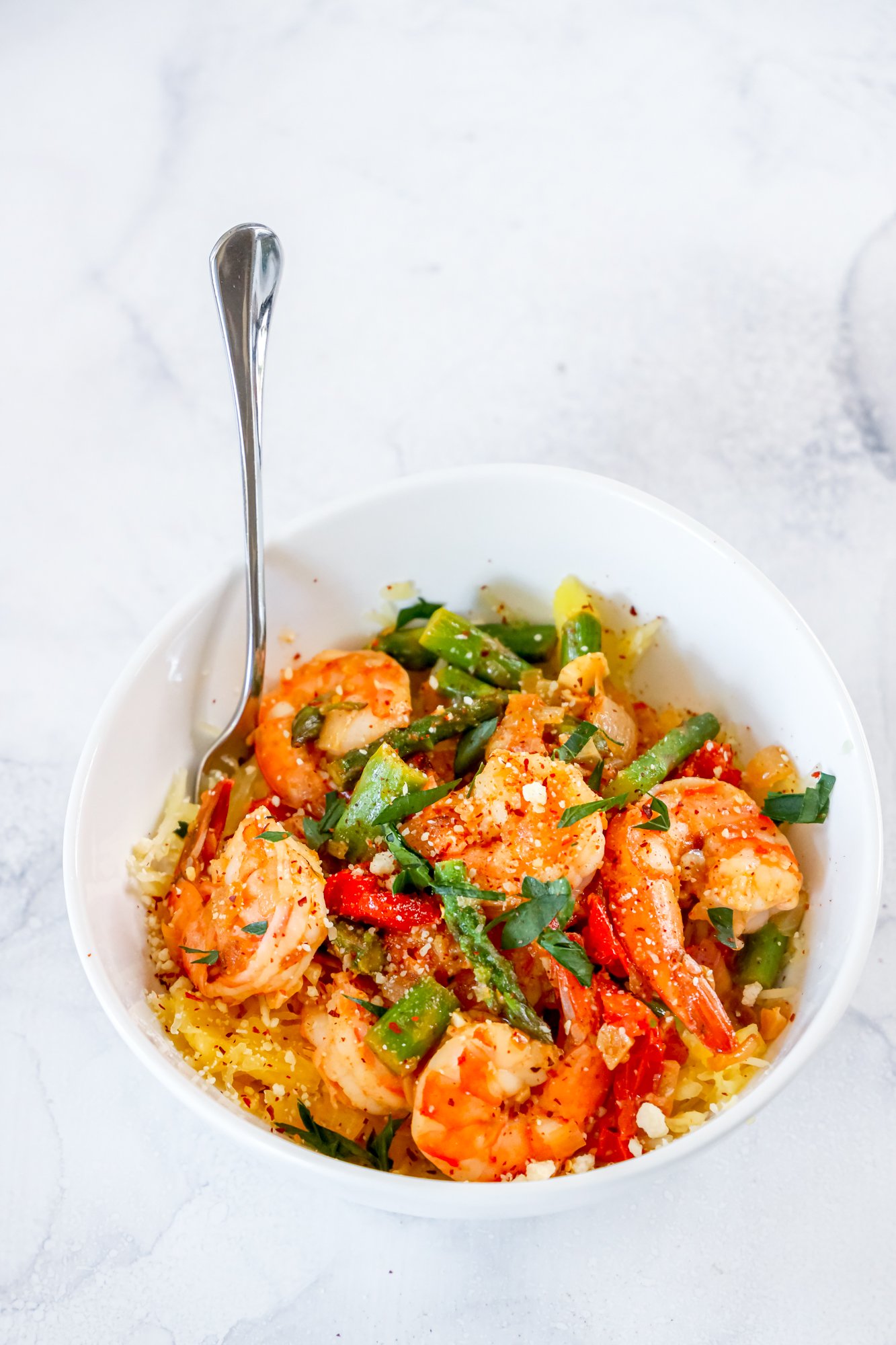 shrimp and asparagus over spaghetti squash noodles in a white bowl 