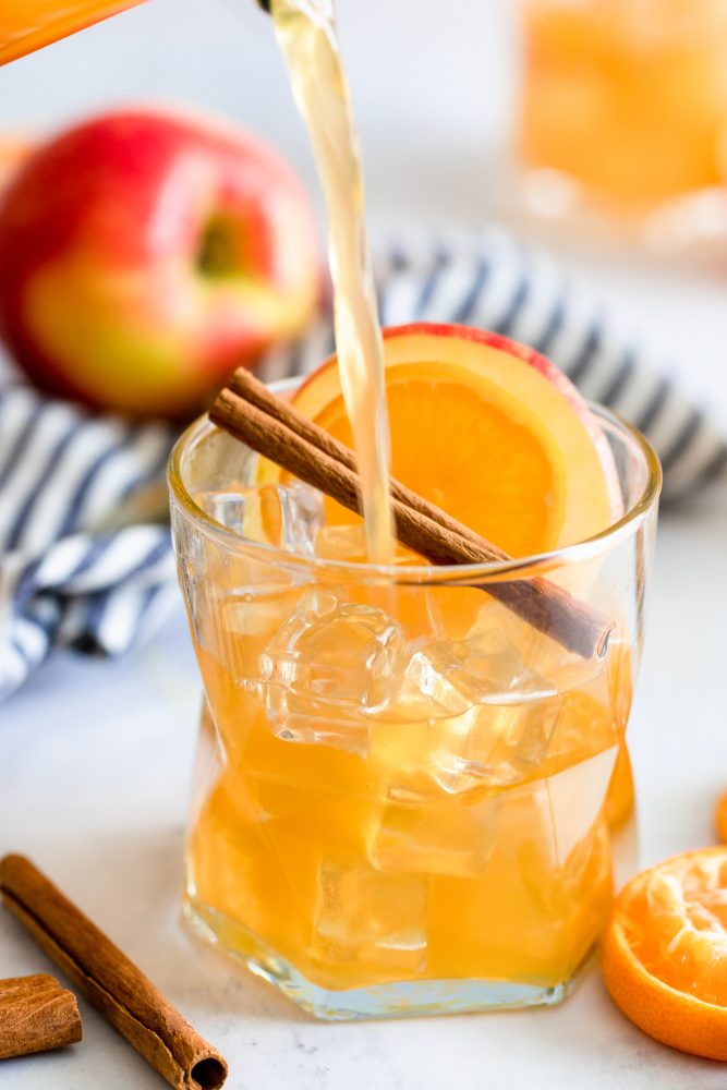 rum punch in a glass with an apple cinnamon stick and slice of orange