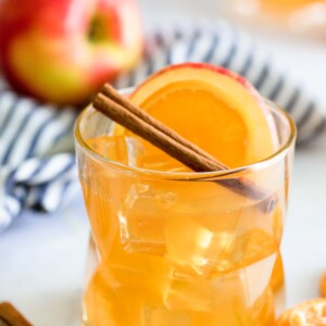 A glass of orange juice garnished with cinnamon sticks and orange slices.