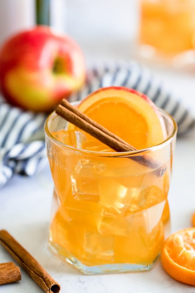 rum punch in a glass with an apple cinnamon stick and slice of orange