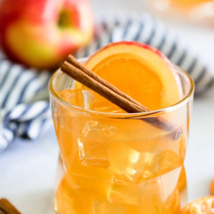 A glass of orange juice garnished with cinnamon sticks and orange slices.