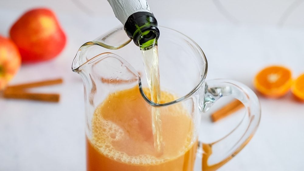 rum punch in a glass with an apple cinnamon stick and slice of orange