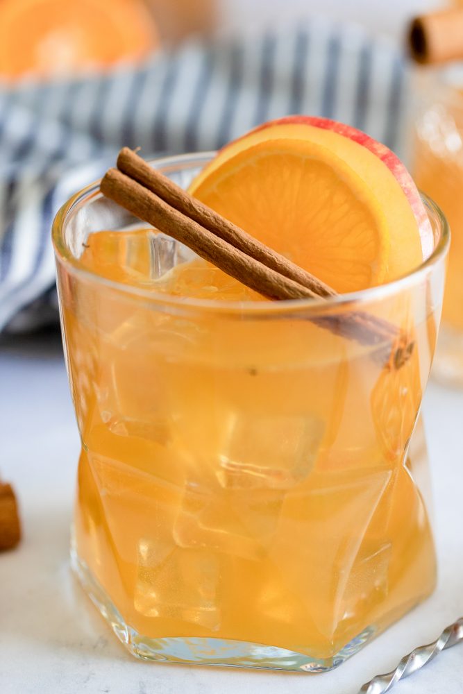 rum punch in a glass with an apple cinnamon stick and slice of orange