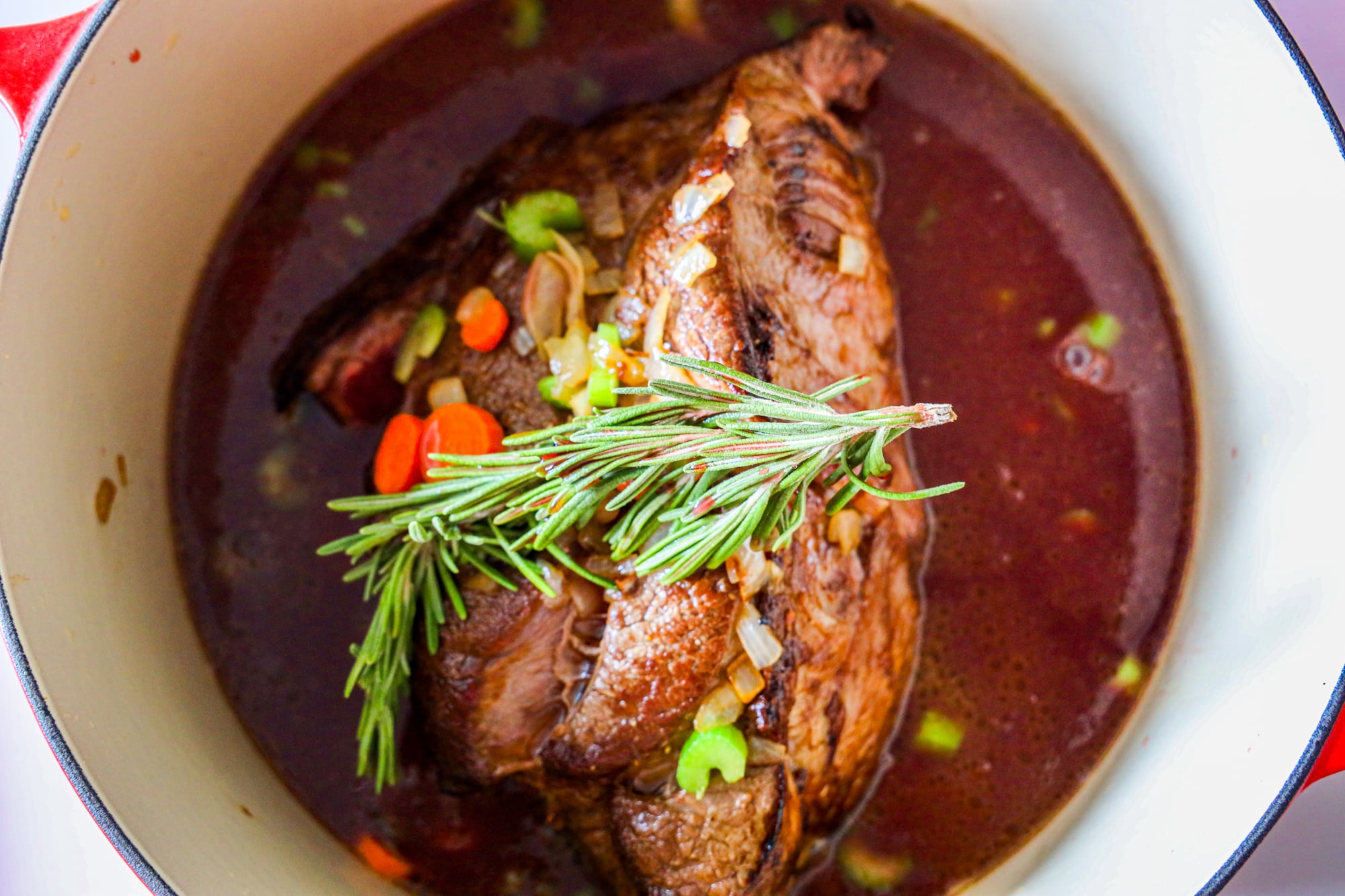 A browned beef roast cooking in a large white pot with visible juices at the bottom.
