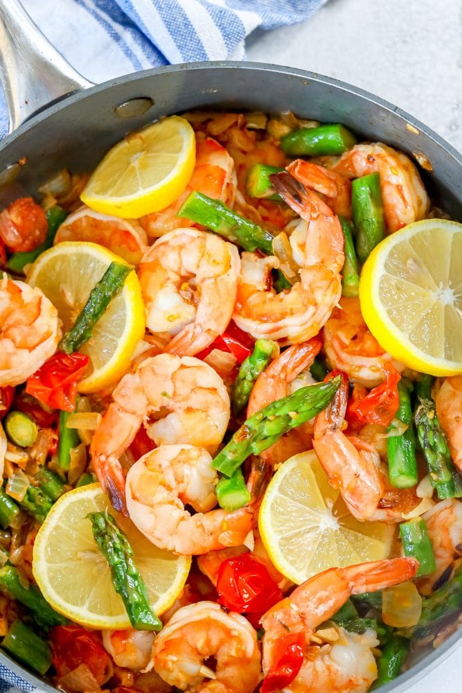 picture of shrimp, asparagus, cherry tomatoes, and lemons in a grey skillet