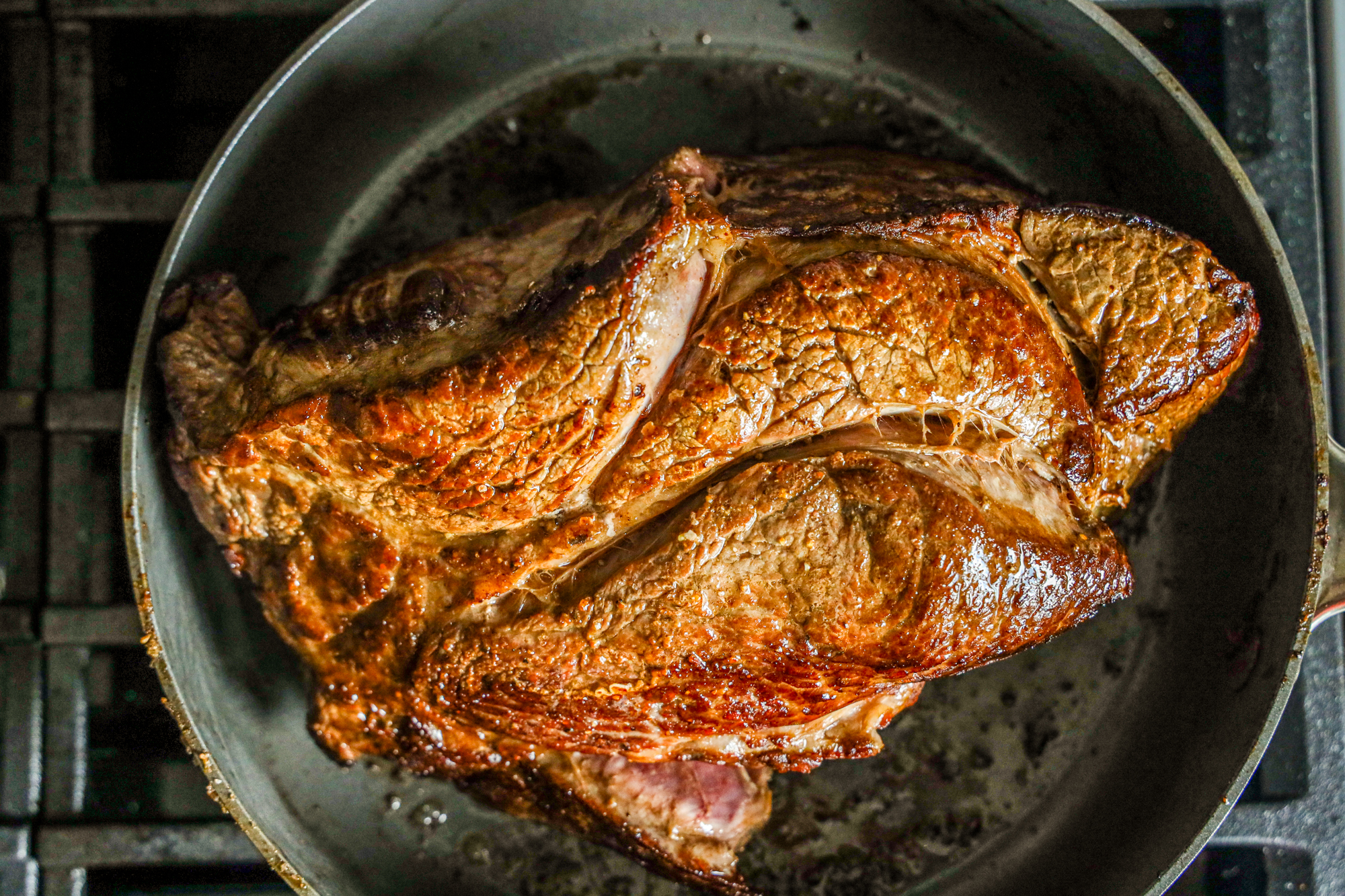 A browned beef roast cooking in a large white pot with visible juices at the bottom.