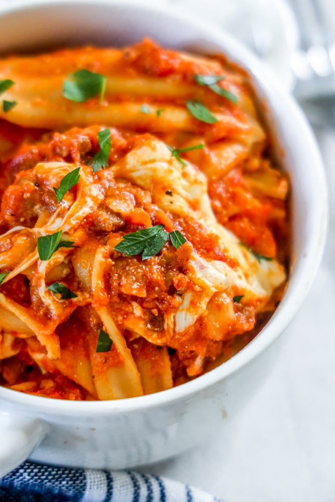 a skillet of lasagna noodles, sauce, and mozzarella cheese with parsley on it