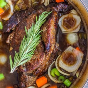 pot roast in a pan with herbs, onions, carrots, and celery