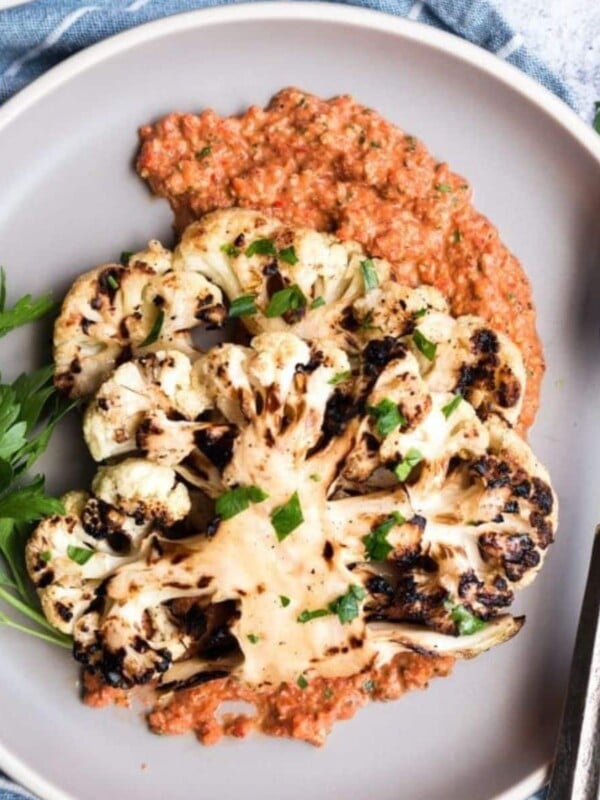 grilled cauliflower steak on a plate with roasted red pepper sauce