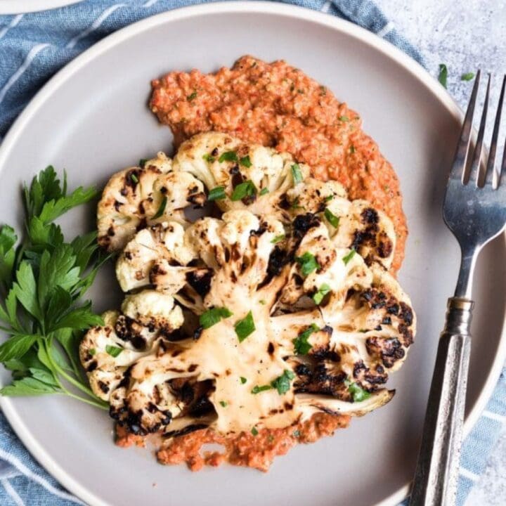 grilled cauliflower steak on a plate with roasted red pepper sauce