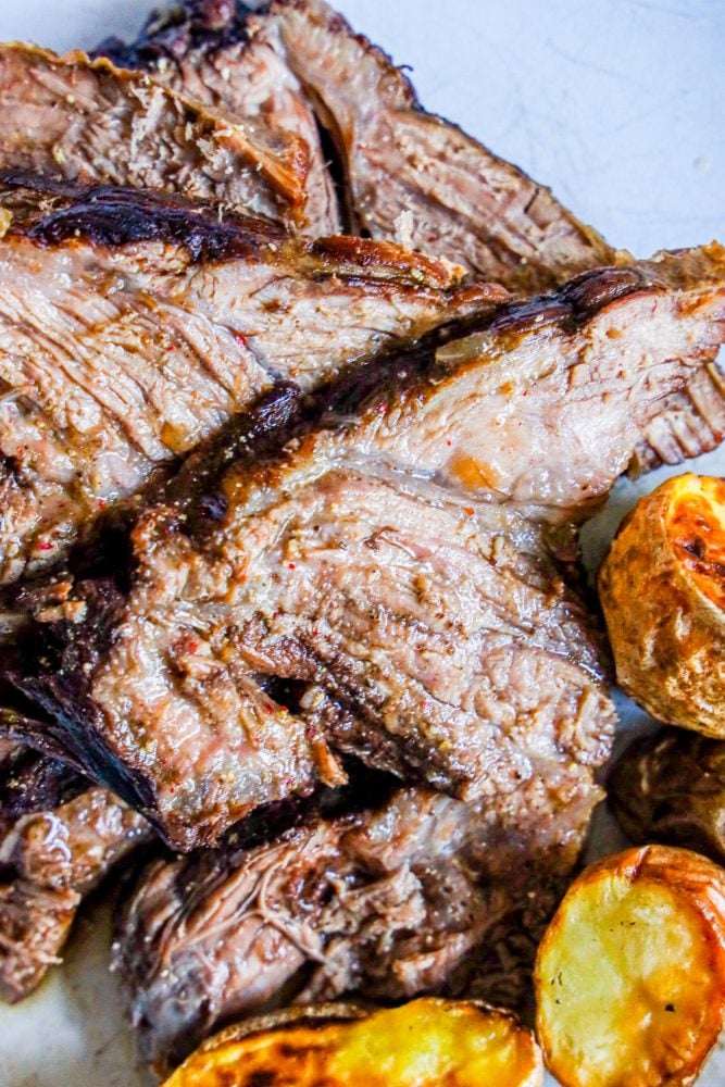 sliced pot roast on a plate with crispy baked potatoes 