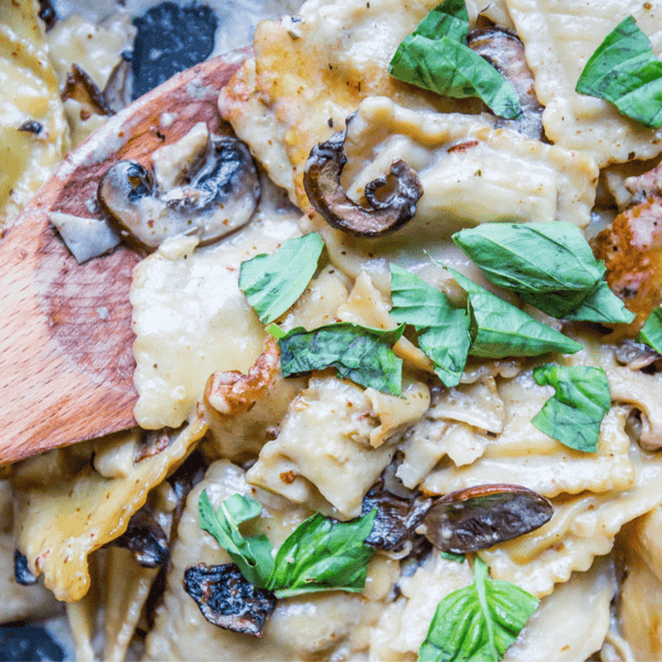 Close-up of creamy mushroom and spinach pasta garnished with fresh basil leaves, mixed and served with a wooden spoon. Try diversifying your meal by exploring our Skillet Ravioli Stroganoff Recipe for a hearty twist on this classic dish.