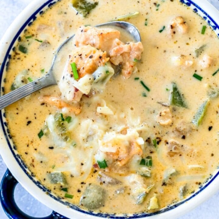 decorative bowl with a spoon scooping white chili with chunks of chicken, chopped bell peppers, flakes of black pepper, and shredded cheese on top