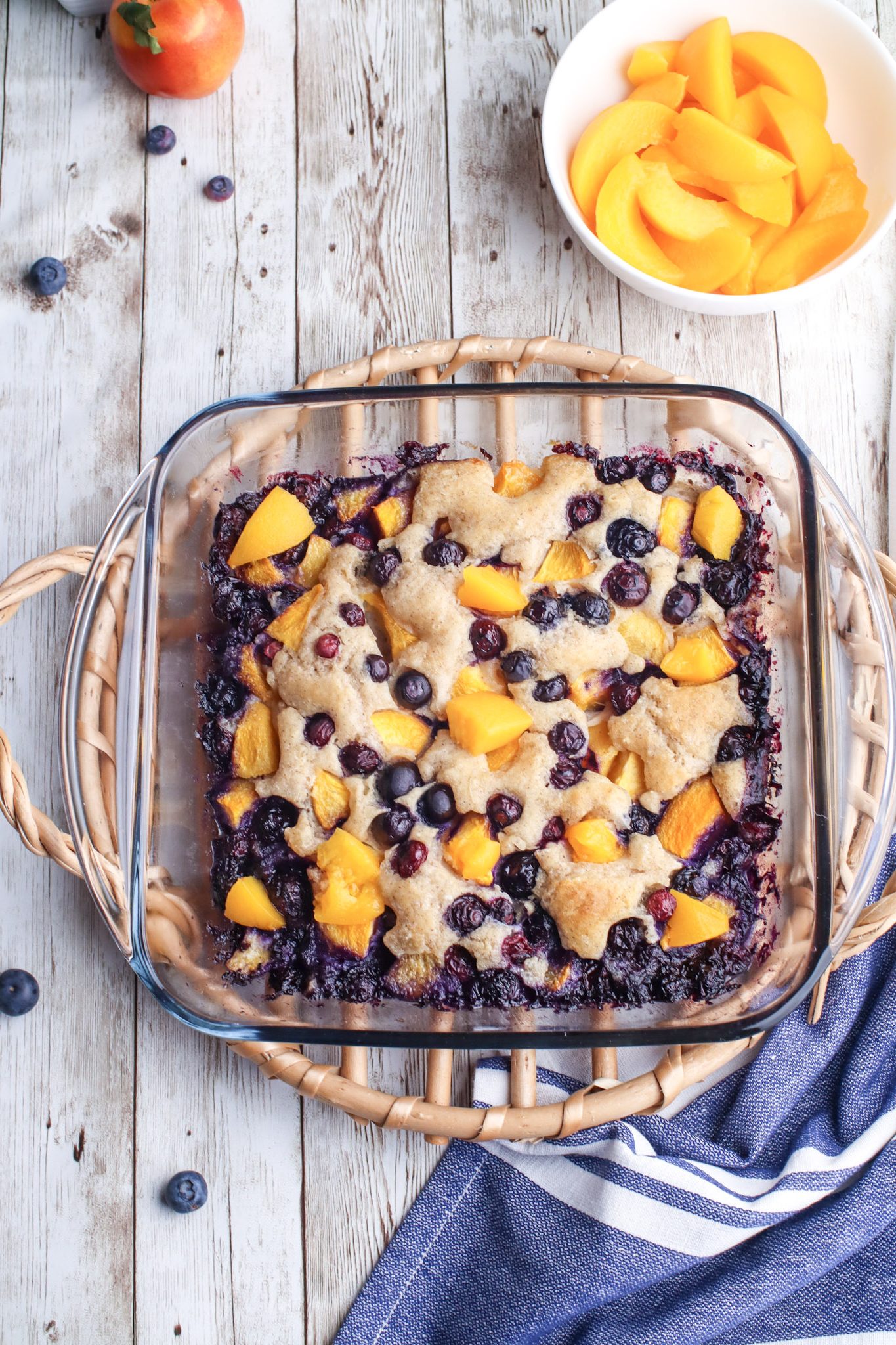 blueberry peach baked cobbler with baked topping on it in a glass pan