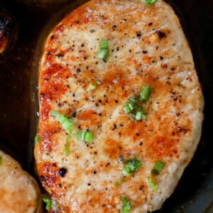 Pork chops cooked in a skillet with garlic butter.