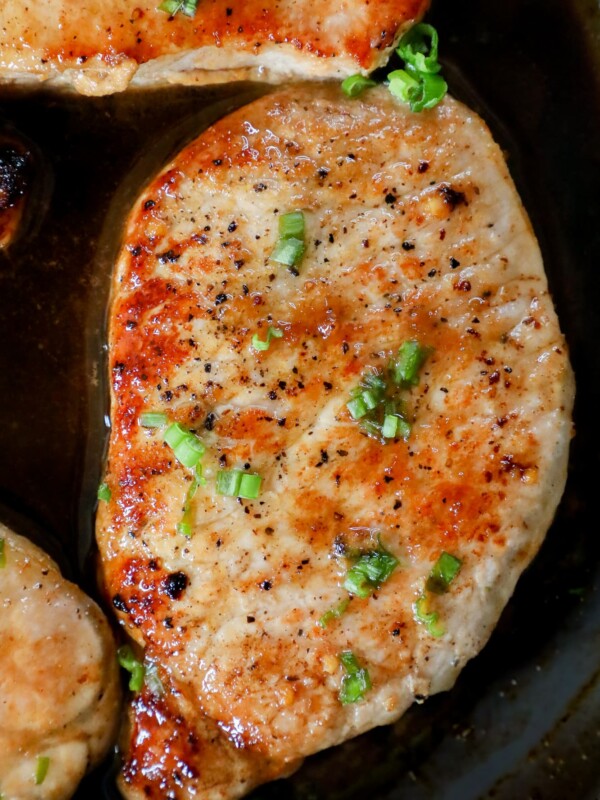 Pork chops cooked in a skillet with garlic butter.