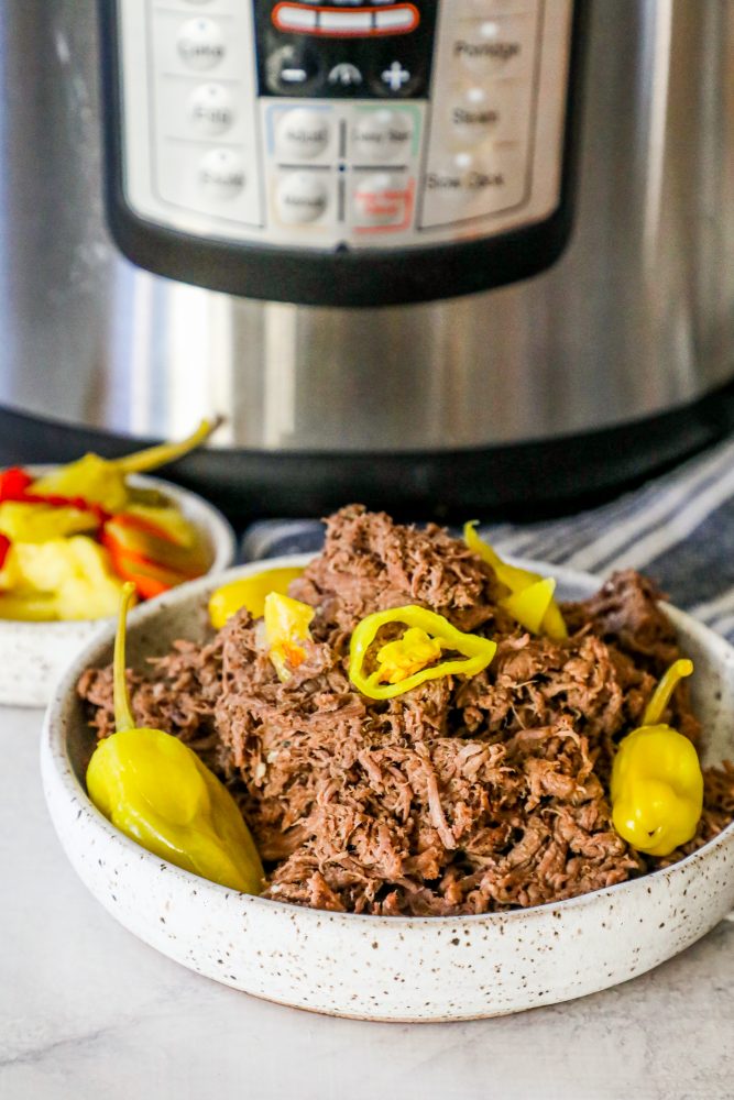 Picture of Italian shredded beef in a white bowl in front of an instant pot