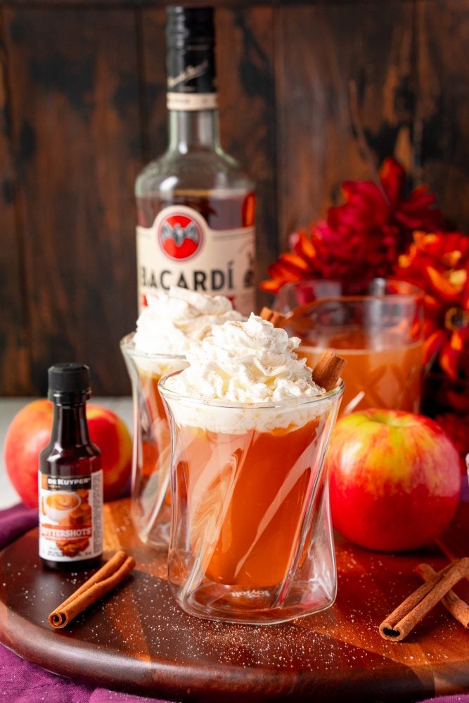 butter rum cider in a glass with whipped cream and cinnamon sticks