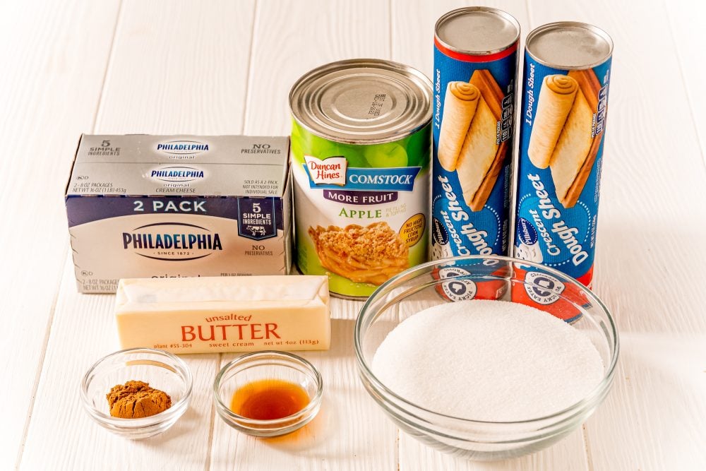 picture of crescent dough cans, cream cheese, apple pie filling, butter, cinnamon, sugar, and butter on a table