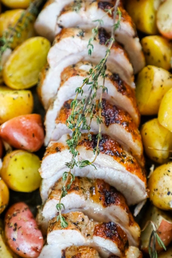 picture of baked pork loin in a pan with seasoned potatoes and onions and a sprig of rosemary