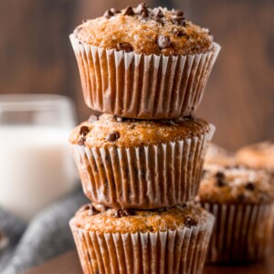 A stack of delicious chocolate chip muffins on a rustic wooden cutting board.